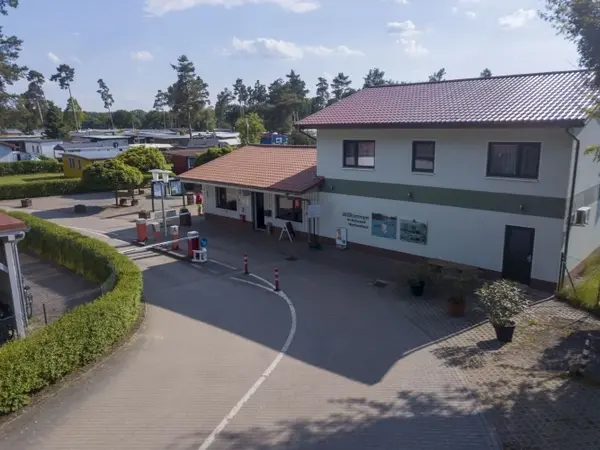 Eingangsbereich eines Campingplatzes mit Rezeption, Schranke und umliegenden Stellplätzen.