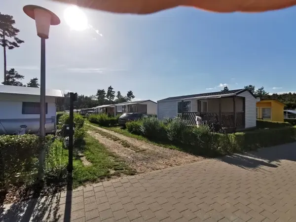 Reihen von modernen Mobilheimen auf einem sonnigen Campingplatz mit viel Grün und Auto.
