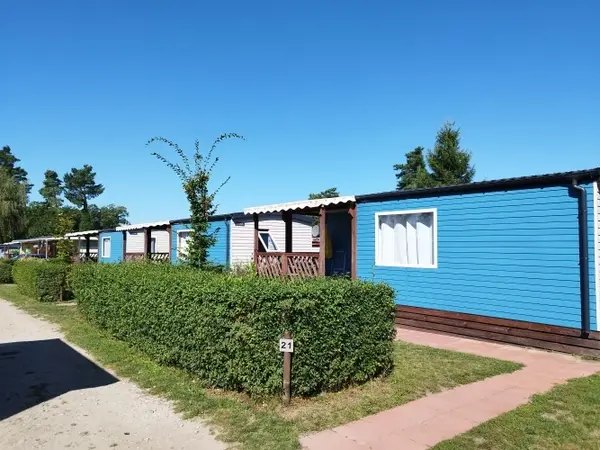 Reihen von blauen Mobilheimen auf einem Campingplatz mit gepflegten Hecken und Sonnenschein.
