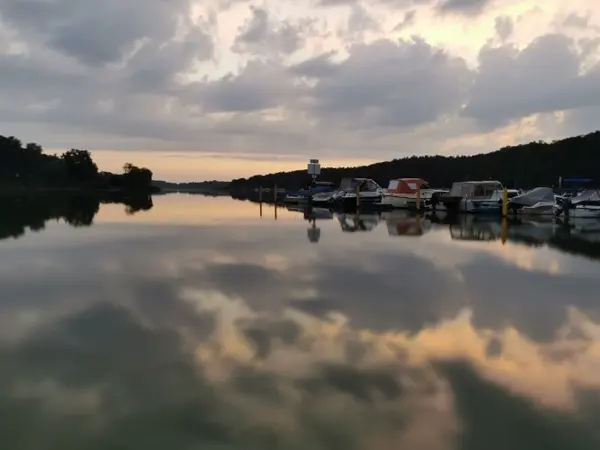 Boote liegen am ruhigen Seeufer, umgeben von Bäumen und einer malerischen Abendstimmung.