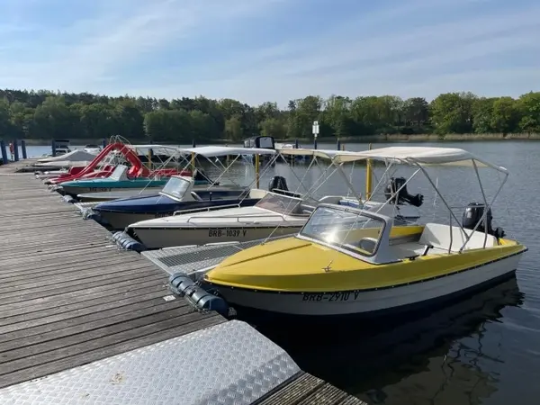 Mehrere Motorboote liegen an einem Holzsteg am Seeufer, umgeben von Bäumen und Natur.
