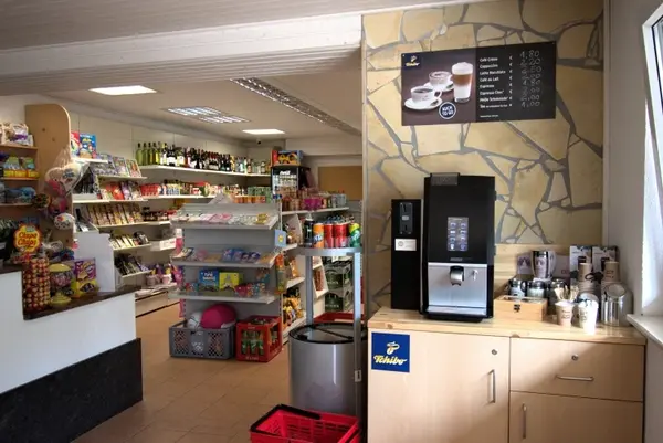 Kleiner Supermarkt mit Kaffeeautomat, Regalen voller Lebensmittel und Getränken im Verkaufsraum.