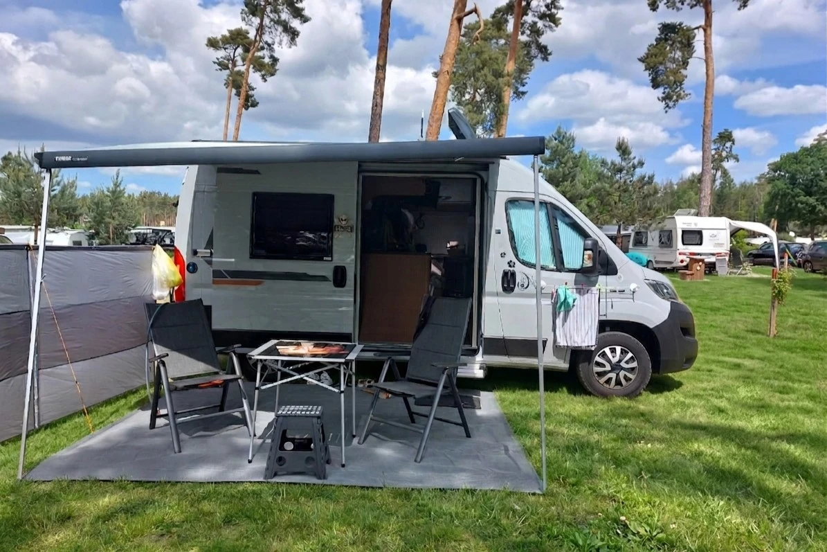 Wohnmobil mit Markise, Tisch und Stühlen auf Campingplatz im Wald