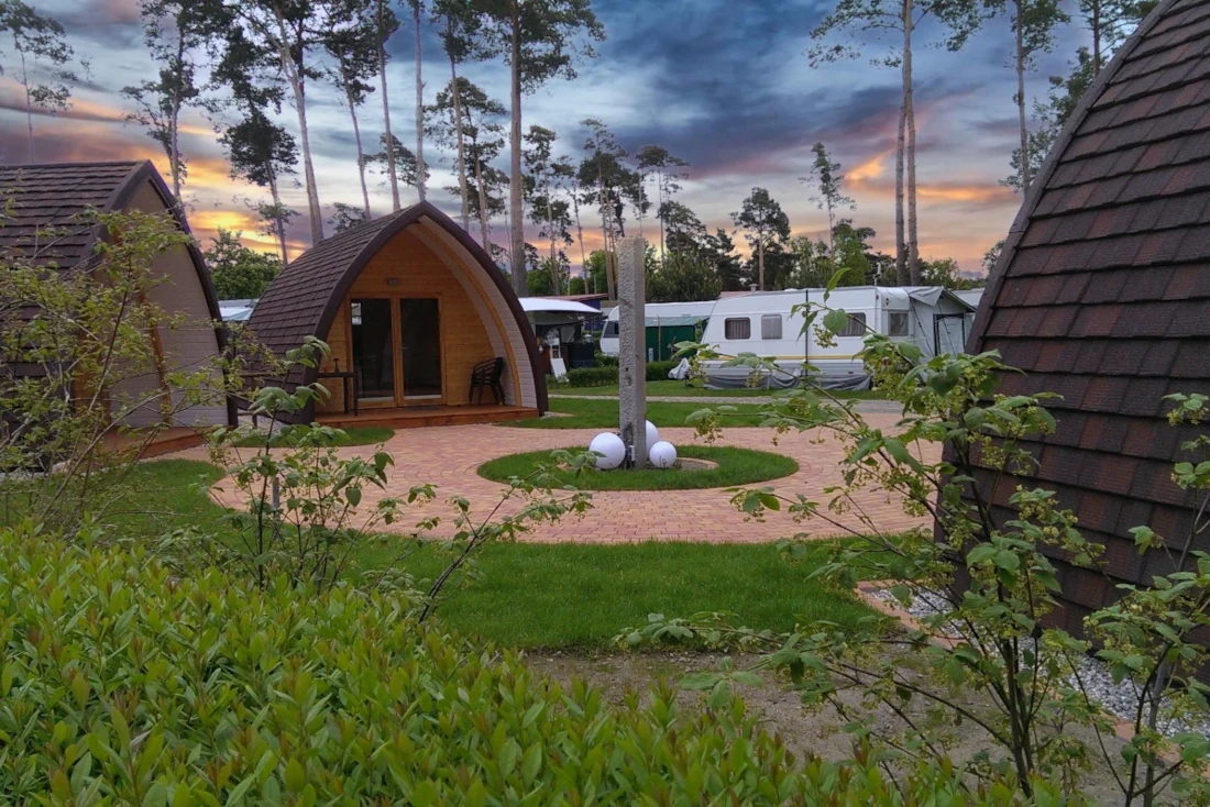 Campingplatz mit Holz-Pods und Wohnwagen im Wald bei Sonnenuntergang